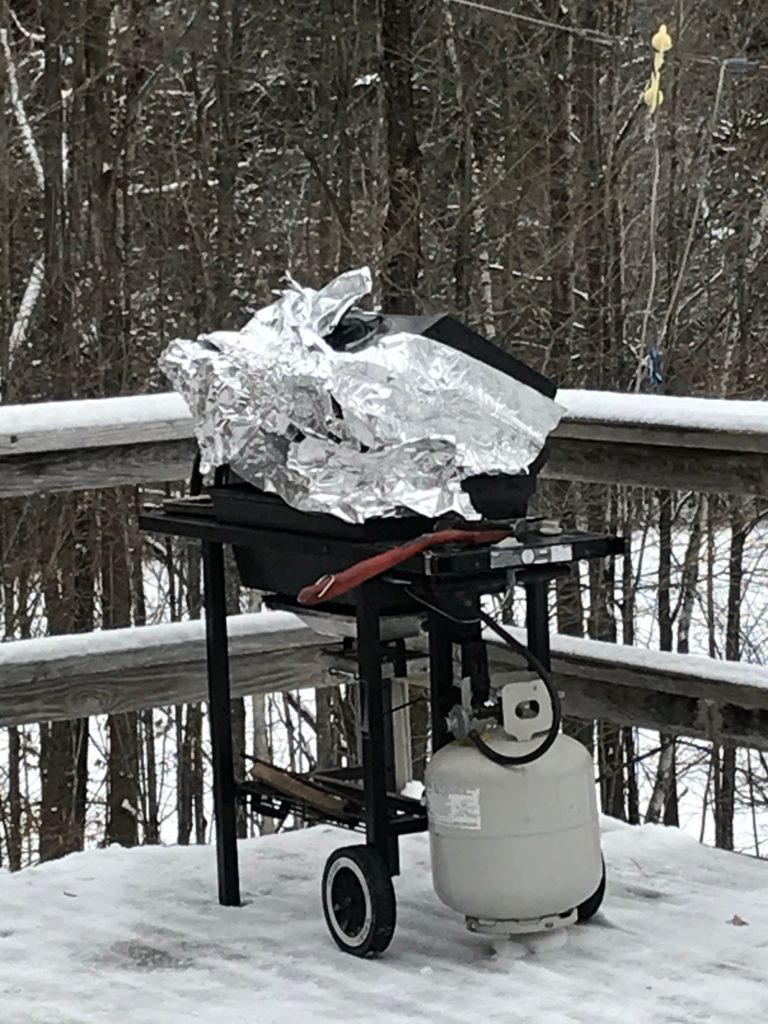 Image showing a black propane gas grill wrapped in tinfoil to preserve heat on snowy deck in winter