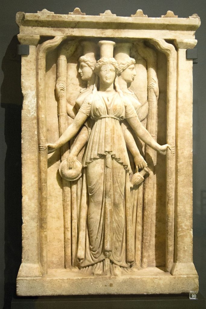 Image of releif of three aspects of goddess Hecate (three women standing back to back, one woman enter) wearing a peplos